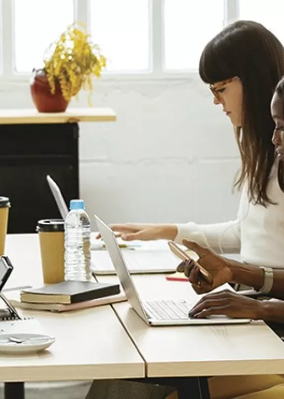 Three workers at communal desk with a printer in the background